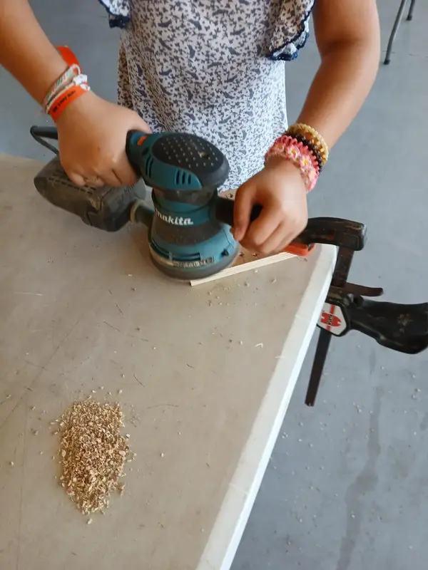 Enfant ponçant une pièce de bois à la ponceuse